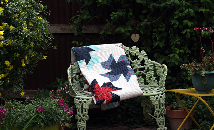 Scrappier Double Pinwheel quilt in a beautiful garden on an iron chair