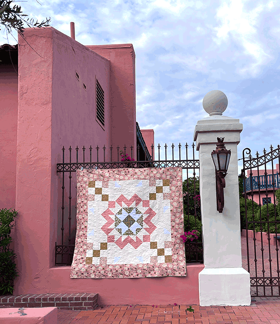 The full quilt top is the focus of this image. It is handing on a rod iron fence. Part of a beautiful building. 